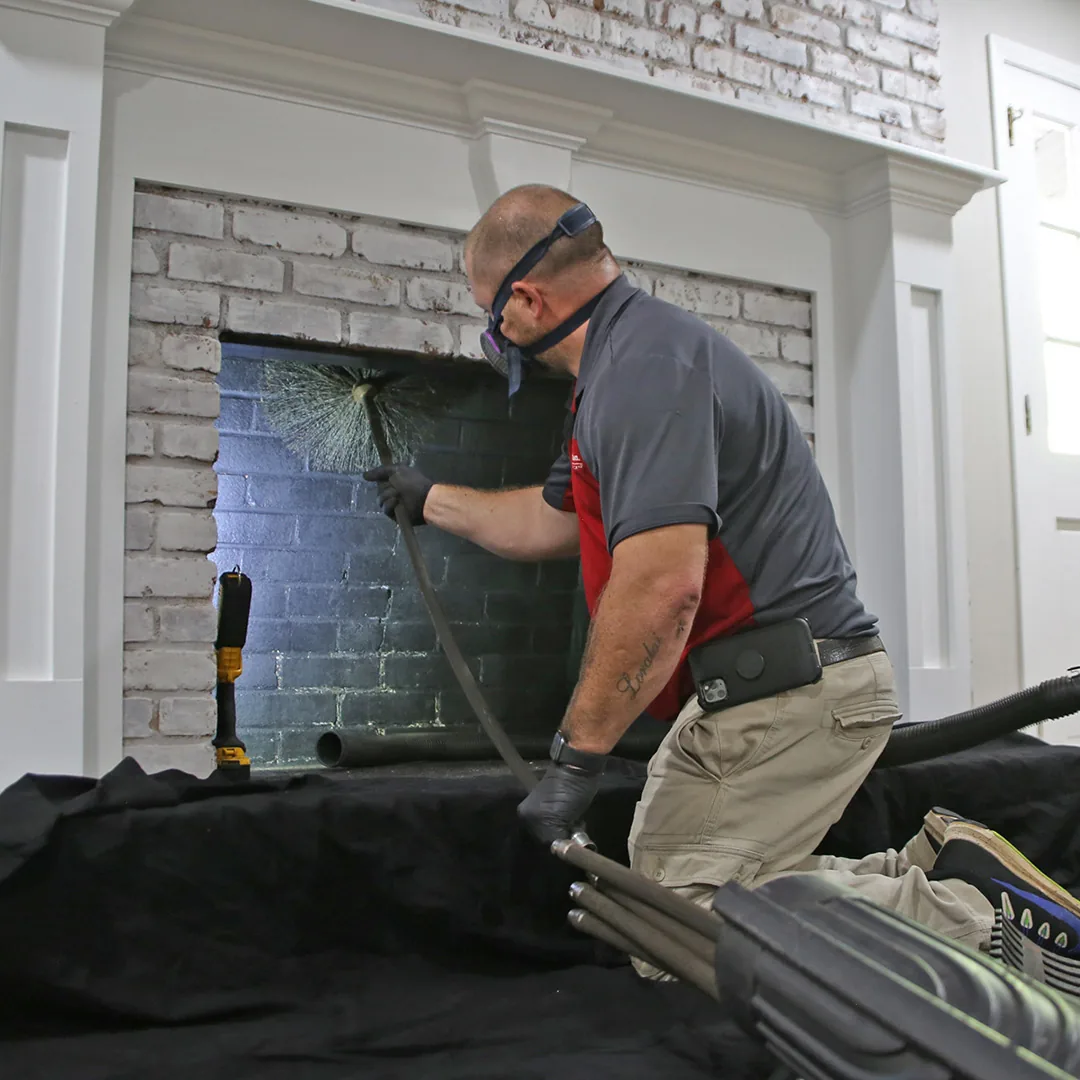 Chimney technician cleaning a residential fireplace with protective floor coverings