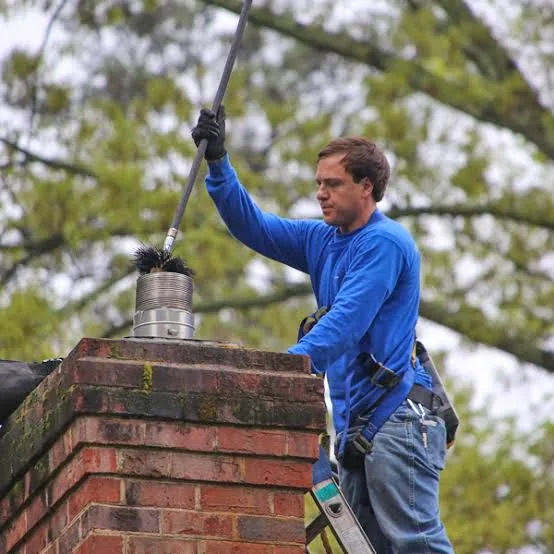 Technician checking a metal chimney cap from a secured rooftop position